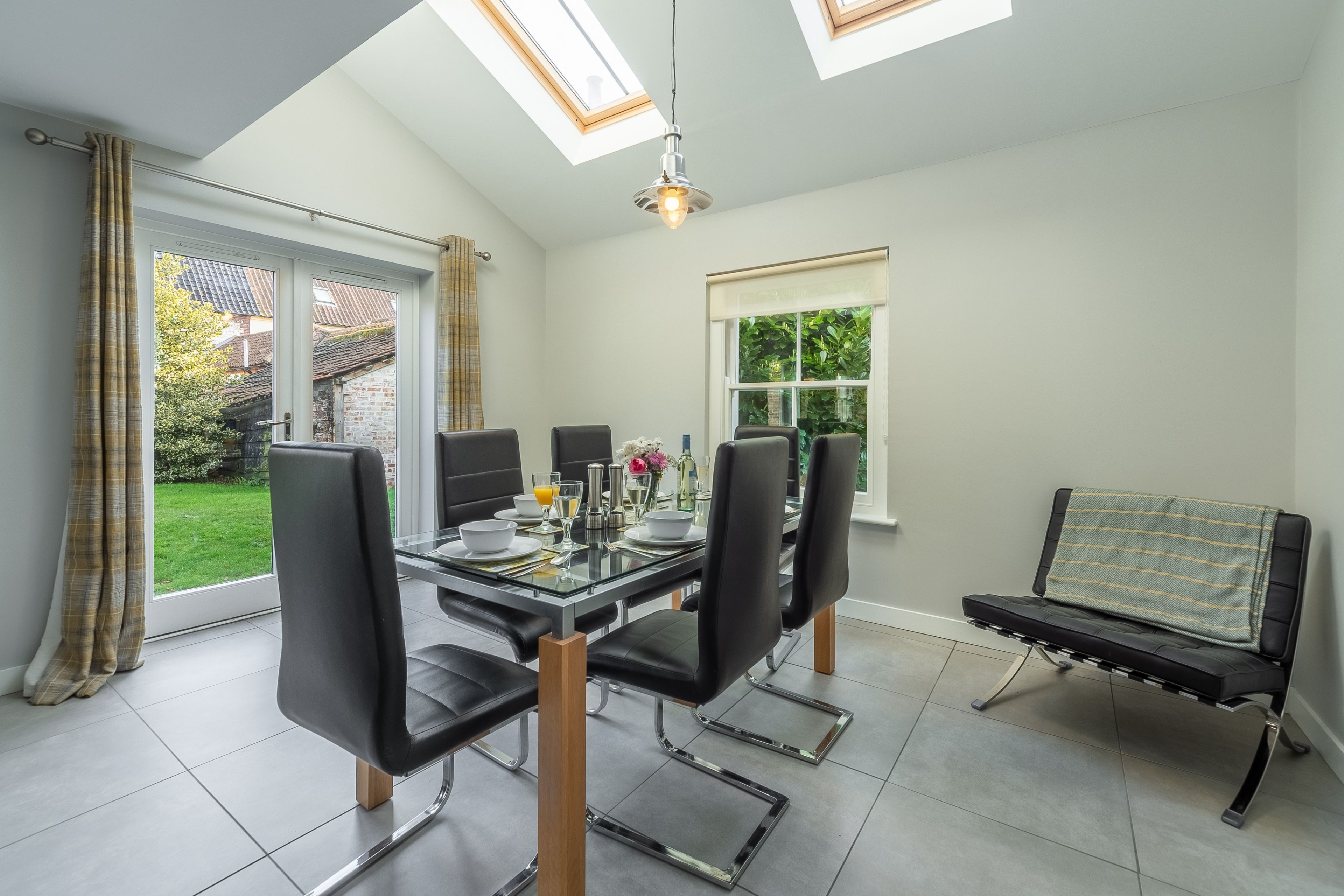 A dining area with a glass table, four black chairs, a bench, and a skylight.