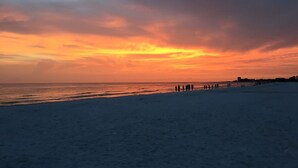 Uma praia com pessoas caminhando pela orla durante o pôr do sol.