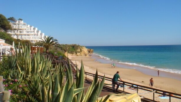 A beach with a wooden walkway, people relaxing, and a building with balconies in the background. -  5min walking distance from amenities and beach , Private Swimming Pool, wifi (Albufeira)