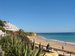 Ein Strand mit einer Holzpromenade, entspannende Menschen und ein Gebäude mit Balkonen im Hintergrund.