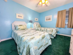 A bedroom with two beds, a nightstand, a lamp, and a window with curtains.