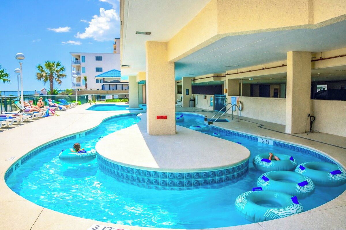 A swimming pool with lounge chairs and inflatable rings, surrounded by a building with a balcony.