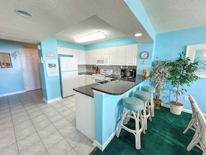 A kitchen with a central island, white cabinets, and a green carpet. - Windy Hill Dunes 105 (North Myrtle Beach)