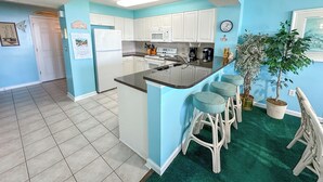 Una cocina con gabinetes blancos, una isla central con taburetes, un microondas y una cafetera.