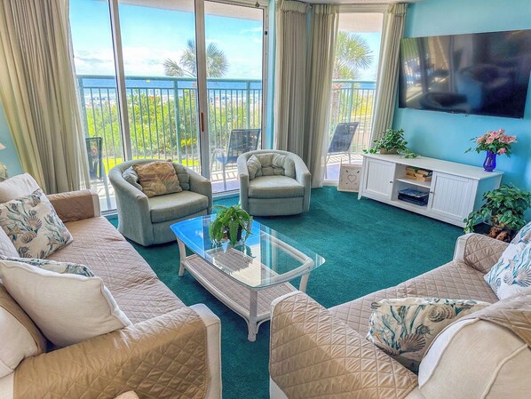 A living room with a glass coffee table, two sofas, a TV, and a view of the outdoors. - Windy Hill Dunes 105 (North Myrtle Beach)