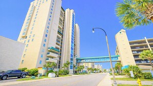 Un hotel de varios pisos con balcones, un puente peatonal y un cielo azul despejado.
