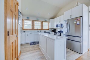 A modern kitchen with white cabinetry, a stainless steel refrigerator, and a wooden door.