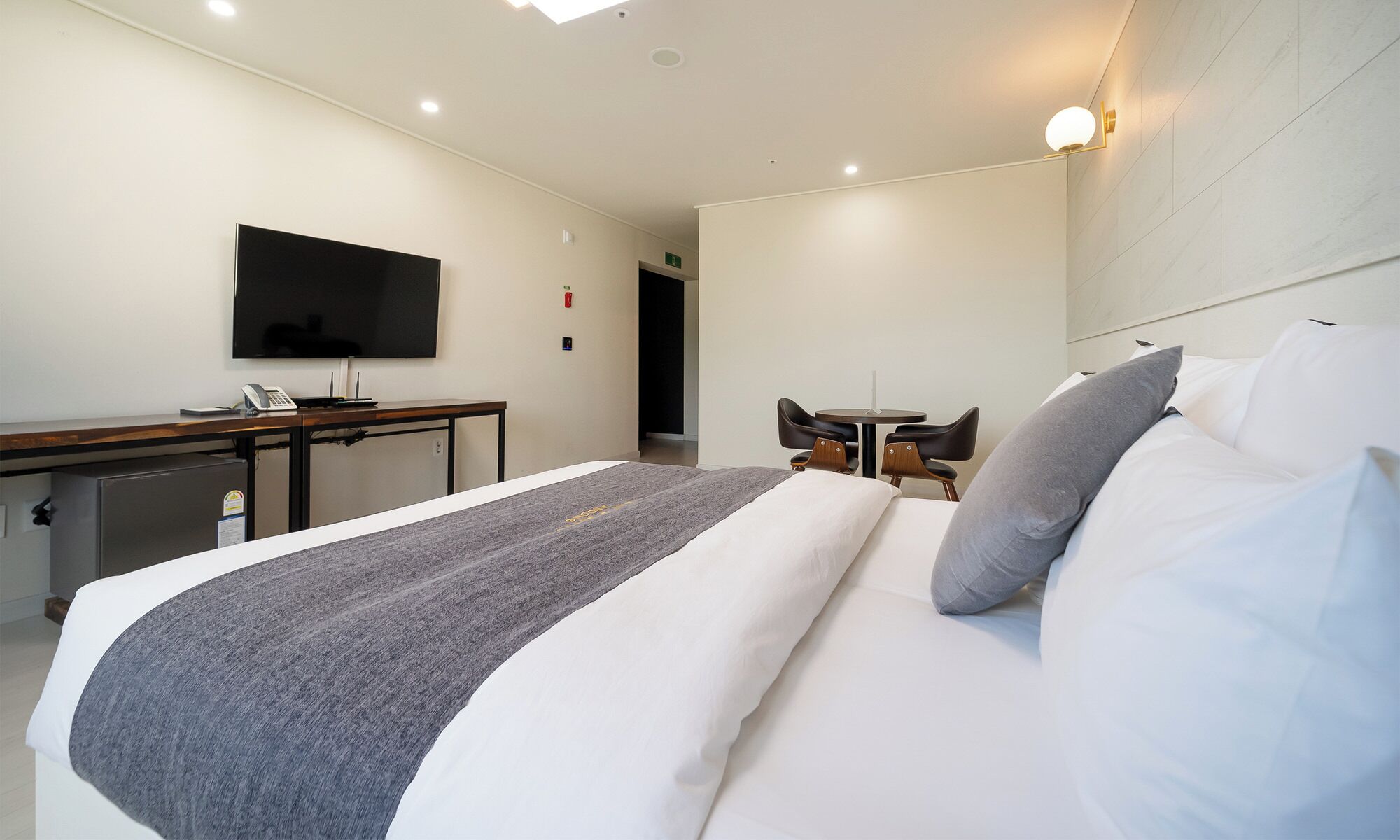Une chambre d’hôtel avec un lit, un bureau, une chaise, une petite table et un téléviseur fixé au mur.