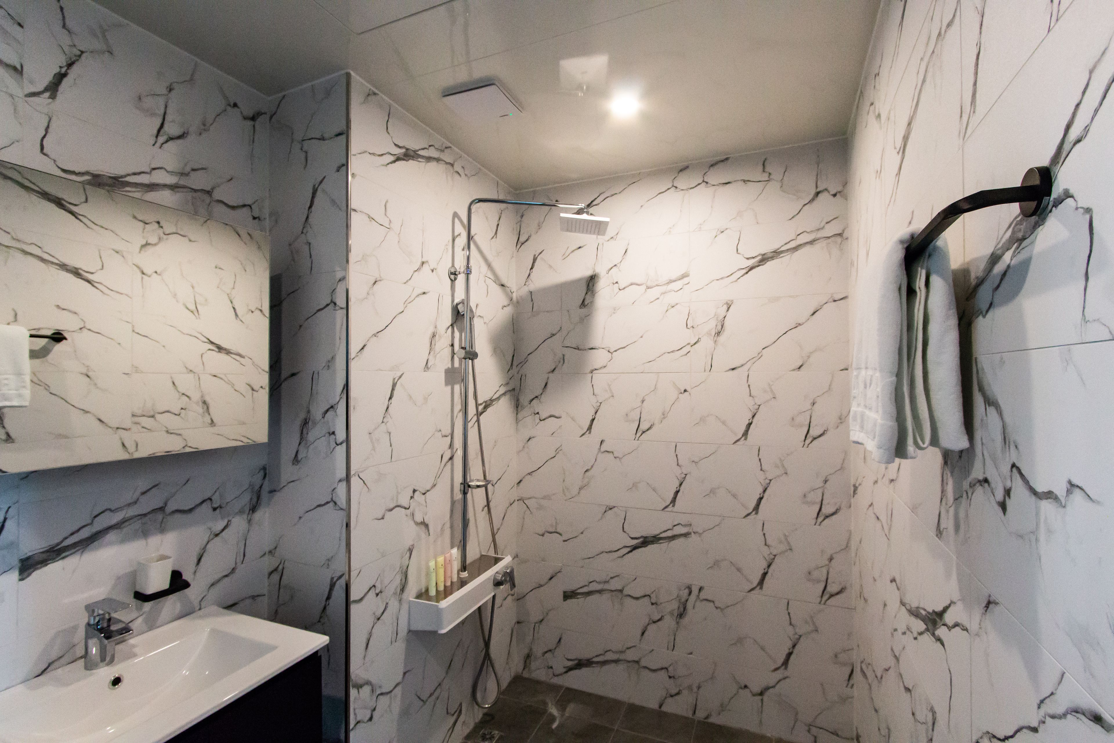 Une salle de bain avec un mur décoré de motifs en marbre, un lavabo et une douche équipée d’un pommeau de douche à main.