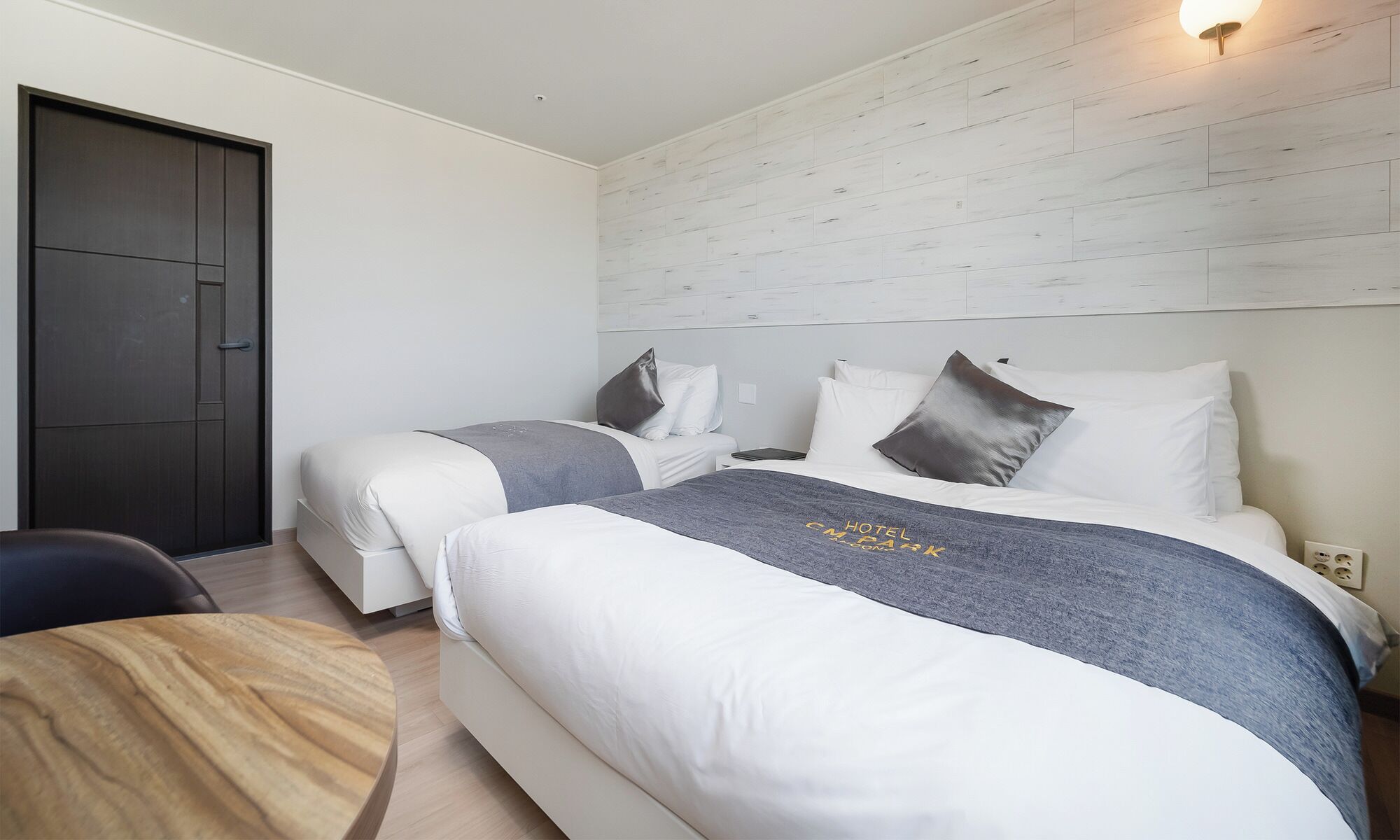 A hotel room with two beds, a wooden table, and a dark door.