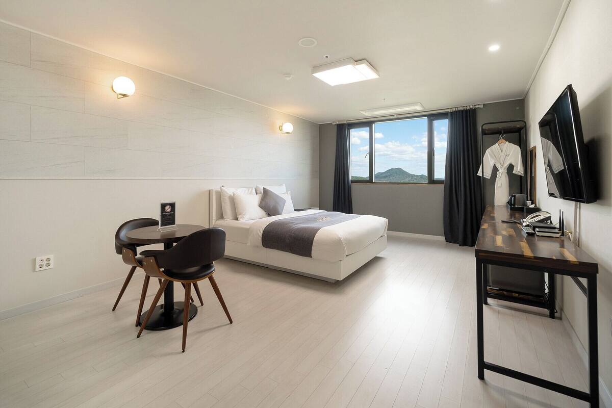Una habitación de hotel moderna con cama, escritorio, silla, televisión y vistas al exterior.