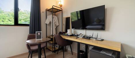 A hotel room with a wooden desk, two chairs, a TV, a small fridge, and a window with curtains.