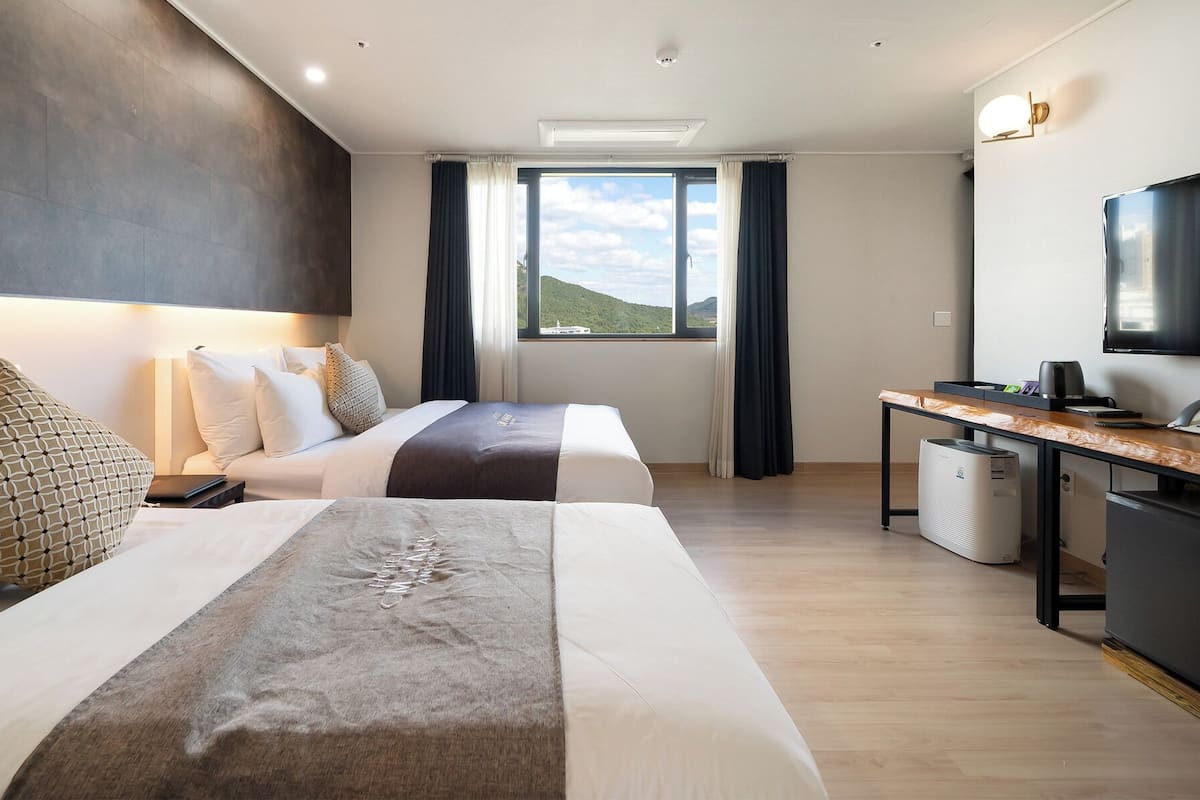 Habitación de hotel con dos camas, un escritorio, un televisor y vistas al exterior.