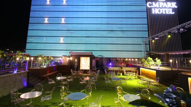 A hotel with a large illuminated sign, outdoor seating area with tables and chairs, and a well-lit entrance. - Andong CM Park Hotel (Yecheon)