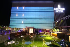 Un hôtel doté d’une grande enseigne lumineuse, d’un espace extérieur aménagé avec des tables et des chaises, et d’une entrée bien éclairée.
