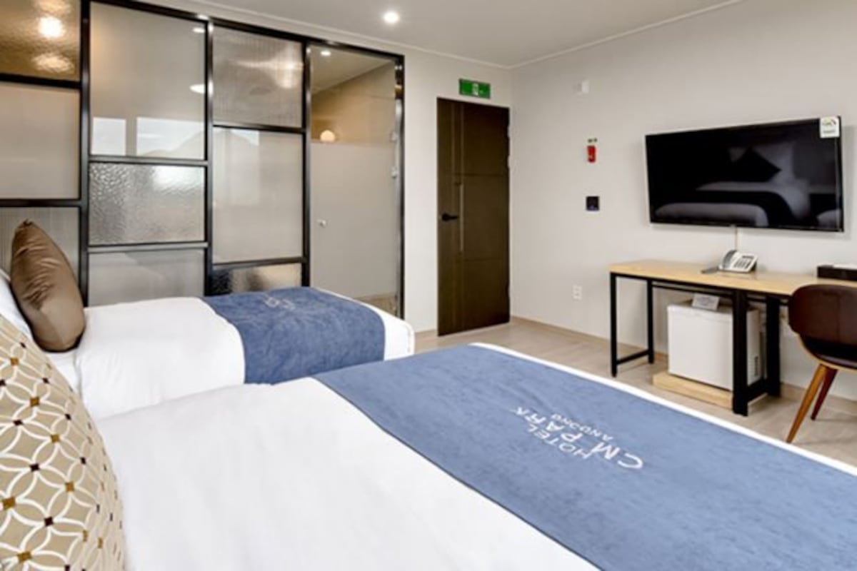 Une chambre d’hôtel avec deux lits, un bureau, une chaise, une télévision et une porte coulissante.
