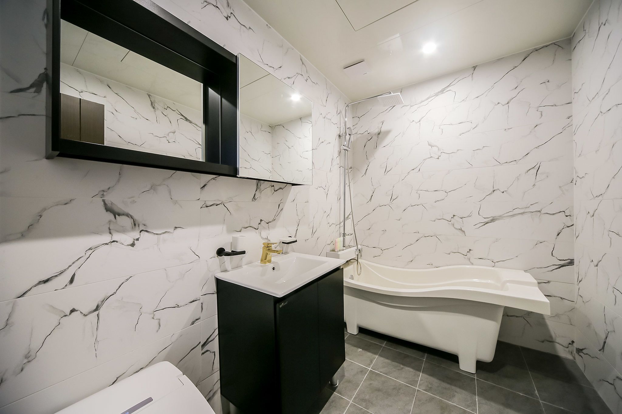 Un bagno moderno con parete in marmo, mobile lavabo nero, lavabo bianco e vasca da bagno bianca, oltre a un grande specchio.