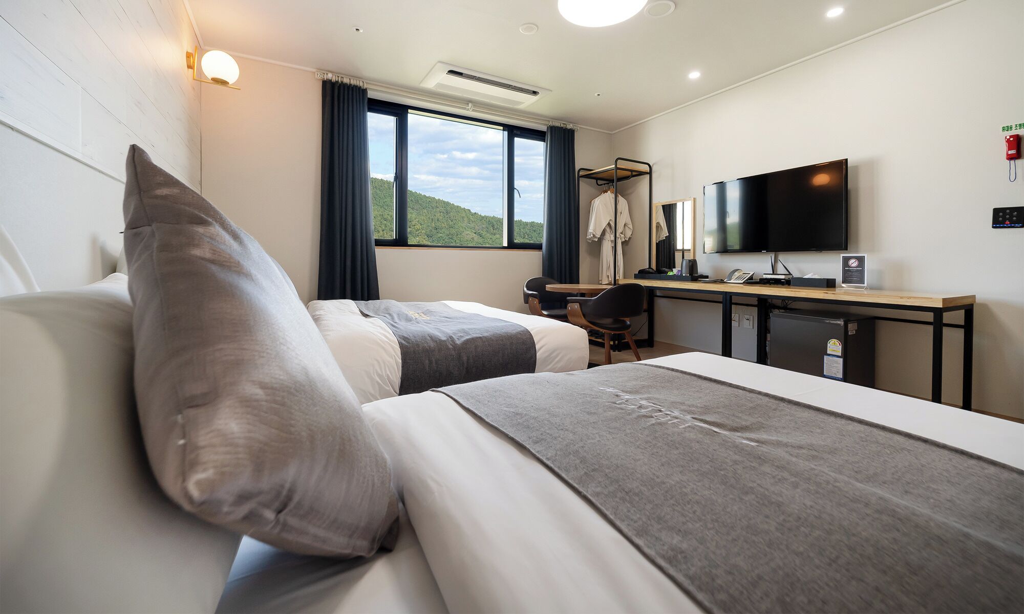 Habitación de hotel con dos camas, un escritorio con televisor y vista al exterior.