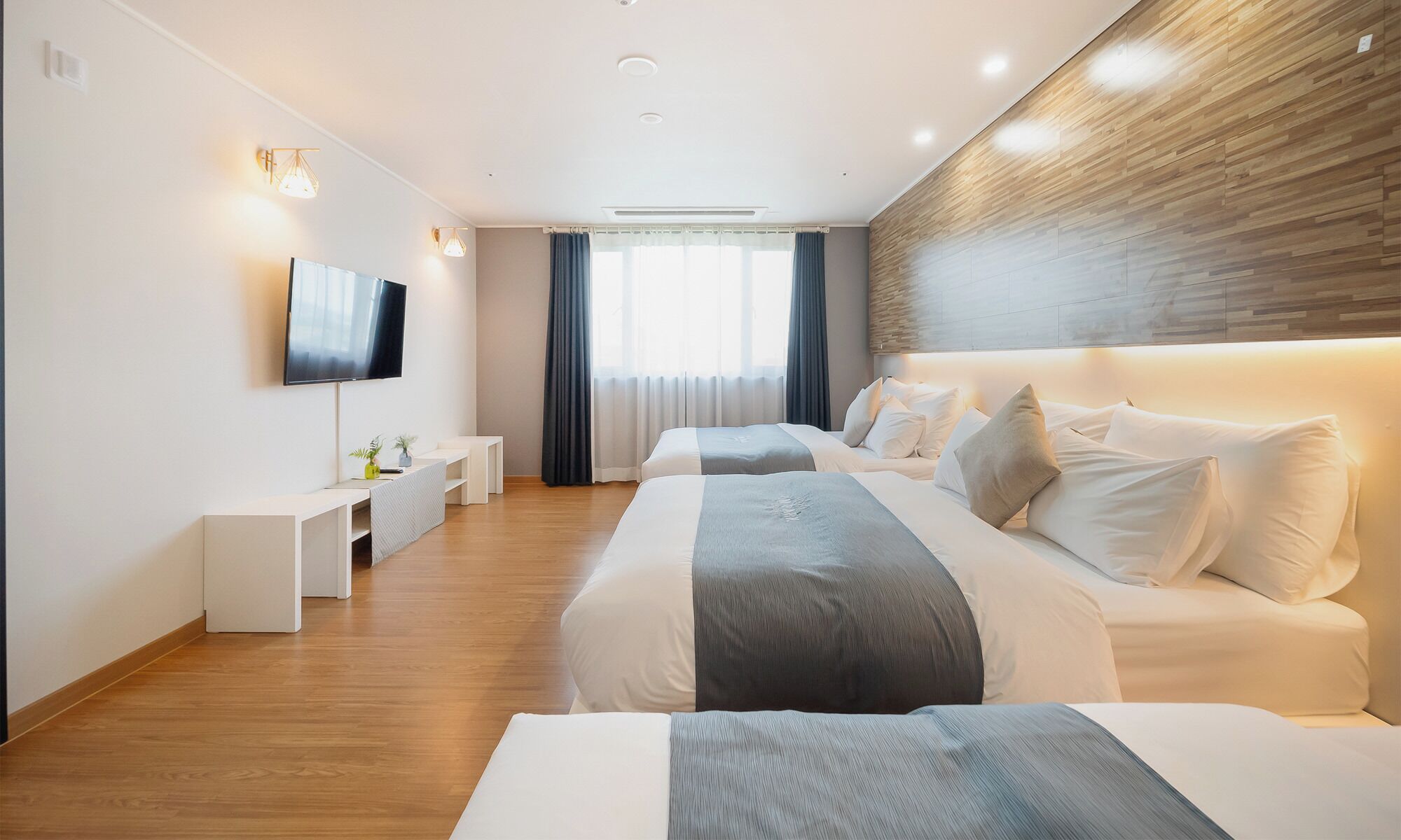 Una habitación de hotel moderna con dos camas, un televisor, un escritorio y un amplio ventanal con cortinas.