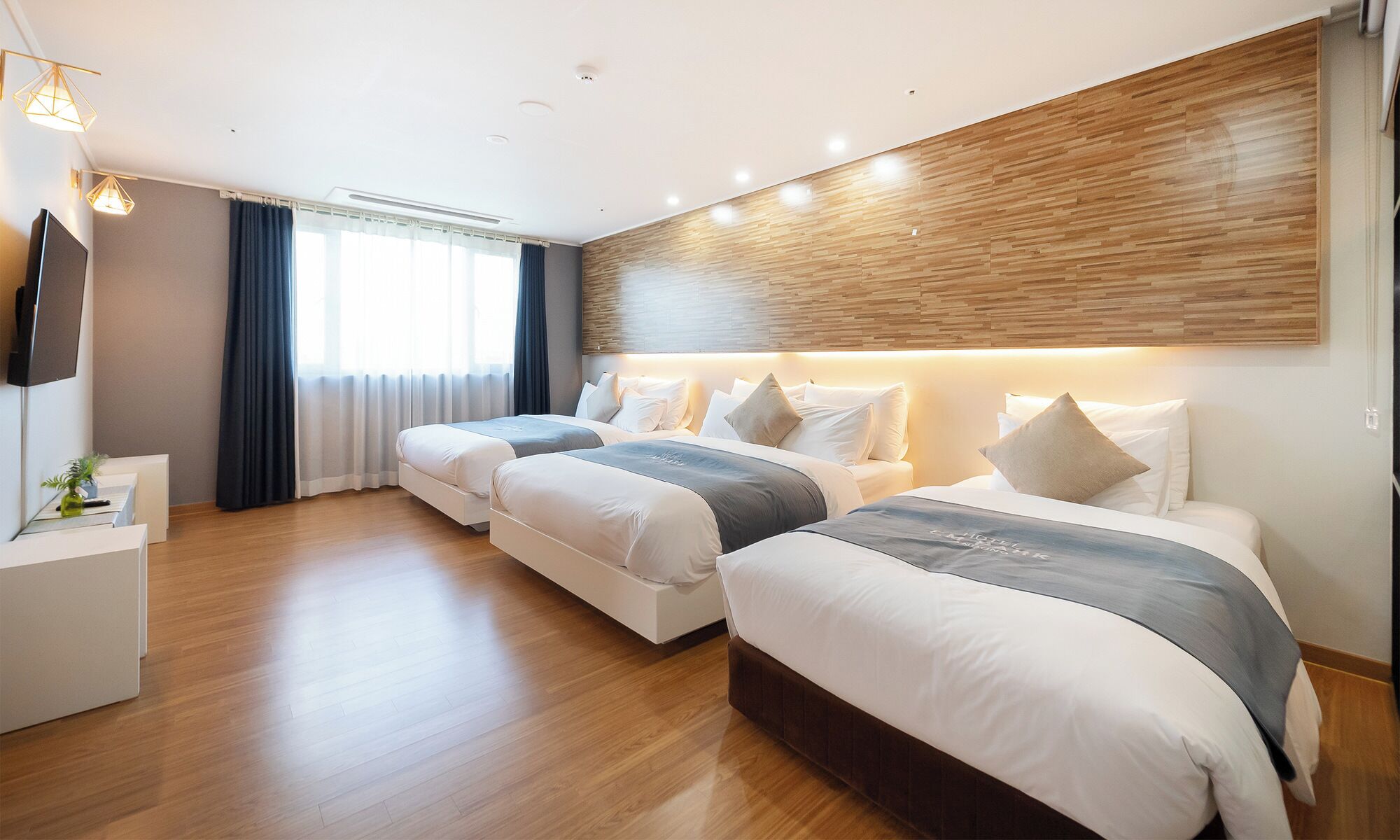 Habitación de hotel con dos camas, televisión, escritorio y ventana grande con cortinas.