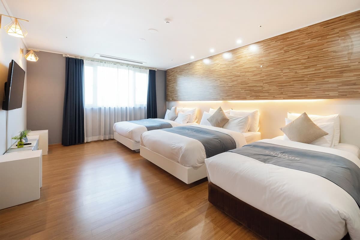 Habitación de hotel con dos camas, televisión, escritorio y ventana grande con cortinas.