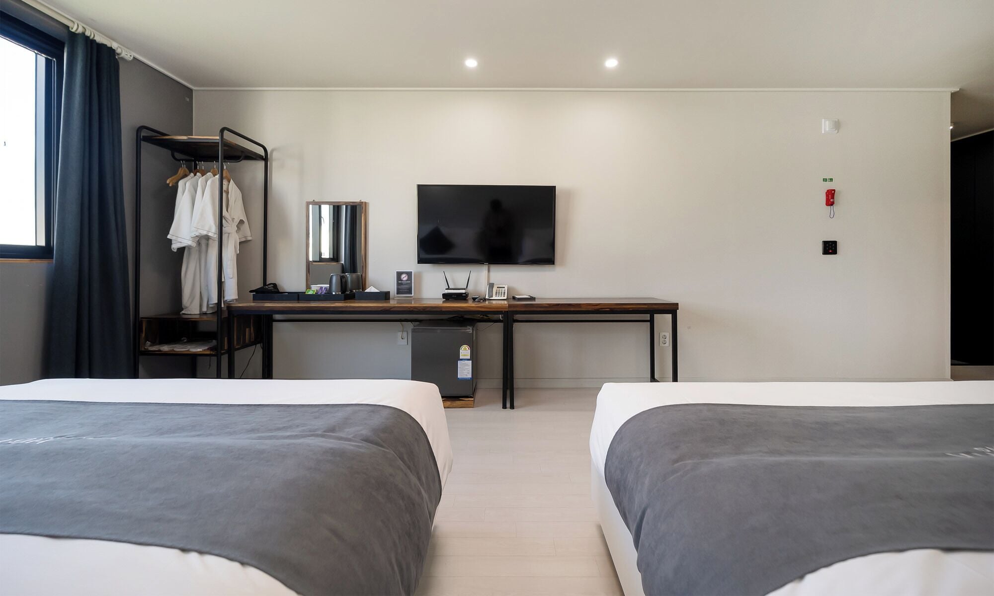 Una habitación de hotel con dos camas, un escritorio, un televisor de pantalla plana, un espejo, un armario y una pequeña cocina.
