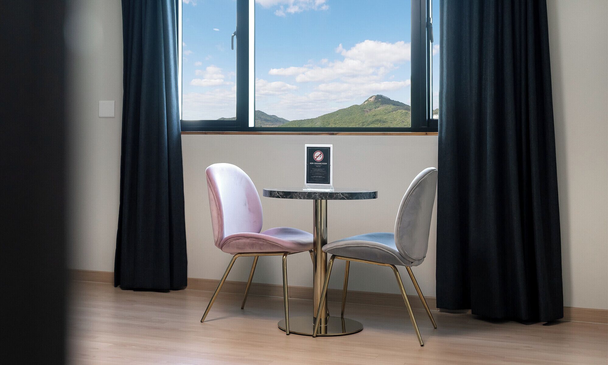 Une chambre avec vue sur la montagne, deux chaises, une petite table et un panneau indiquant qu’il s’agit d’un espace non-fumeur.