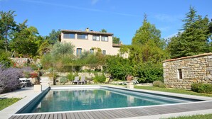 A rectangular swimming pool with a wooden deck, surrounded by lush greenery and a stone wall. - T2 ground floor in Provencal Bastide with swimming pool, heart of the Luberon (Castellet)