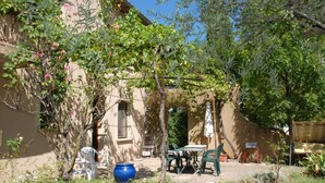 An outdoor patio with a table and chairs, surrounded by greenery and a building. - T2 ground floor in Provencal Bastide with swimming pool, heart of the Luberon (Castellet)