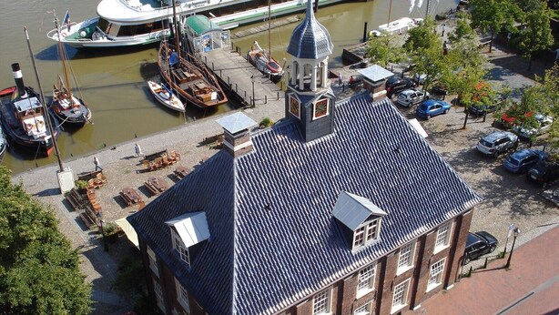 Ein historisches Gebäude mit einem markanten Glockenturm, neben einem Kanal mit Booten.
