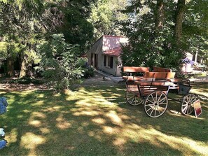A rustic wooden cart with metal wheels in a grassy area with trees and a small building in the background.