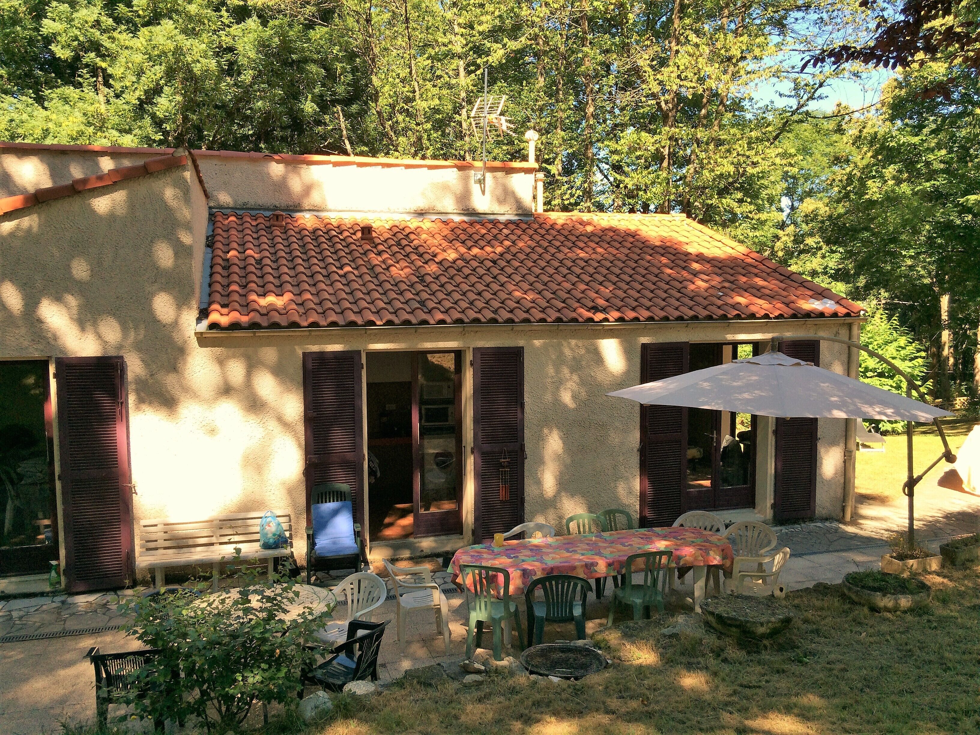 A small house with a tiled roof, a patio with outdoor furniture, and a large umbrella.