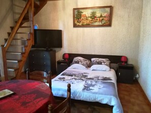 A bedroom with a bed, two bedside tables, a TV, a painting, a chair, and a table.
