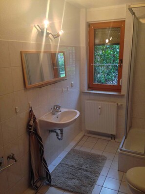 Badezimmer mit Fenster. Ausgestattet mit Dusche, Waschbecken und WC.