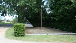 Une zone pavée avec un lampadaire, entourée de verdure et d’une haie.