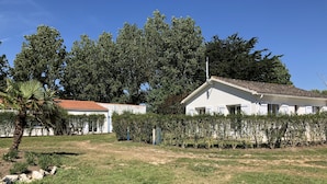 A white building with a tiled roof, surrounded by a well-maintained lawn and a variety of trees. - --Gite Les Courlis-- (Le Perrier)