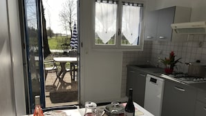 A kitchen with a dining table set for two, a bottle of wine, and a pitcher of water. - --Gite Les Courlis-- (Le Perrier)