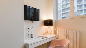 Un espacio de oficina moderno con un escritorio blanco, una silla rosa, un televisor montado y una lámpara de pared.