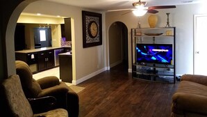 Un salon doté d’un parquet en bois foncé, d’un téléviseur et d’un ventilateur de plafond.