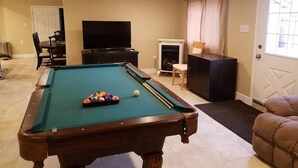 Une table de billard avec des billes, un téléviseur, une cheminée et une porte avec une fenêtre.