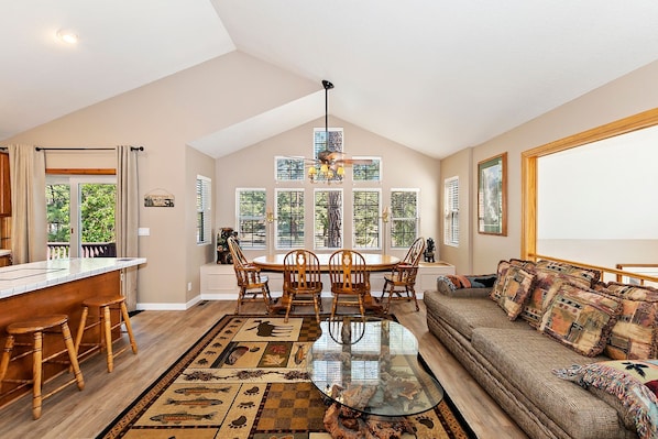 A spacious living area with a dining table, chairs, a glass coffee table, and a sofa with patterned cushions.