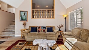 A cozy living room with a sofa set, a coffee table, and a staircase leading to an upper level. - PET FRIENDLY! Expansive Game Room with Pool Table, Ping Pong, Air Hockey & more! HOT TUB! Walk to Lake! (Big Bear Lake)