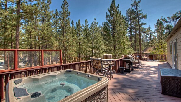 A hot tub on a wooden deck with a view of pine trees. - PET FRIENDLY! Expansive Game Room with Pool Table, Ping Pong, Air Hockey & more! HOT TUB! Walk to Lake! (Big Bear Lake)