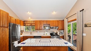 A modern kitchen with wooden cabinets, stainless steel appliances, a tiled island with stools, and a view to the outside. - PET FRIENDLY! Expansive Game Room with Pool Table, Ping Pong, Air Hockey & more! HOT TUB! Walk to Lake! (Big Bear Lake)