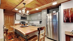 A modern kitchen with a wooden island, stainless steel appliances, and a unique chandelier.