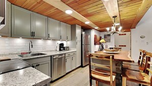 Een moderne keuken met granieten aanrechtbladen, roestvrijstalen apparatuur en houten balken in het plafond.