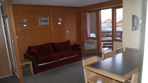A cozy room with a wooden wall, a red sofa, a wooden dining table, and chairs. - APARTMENT ALPE D'HUEZ 6 people BEAR WHITE (L'Alpe d'Huez)