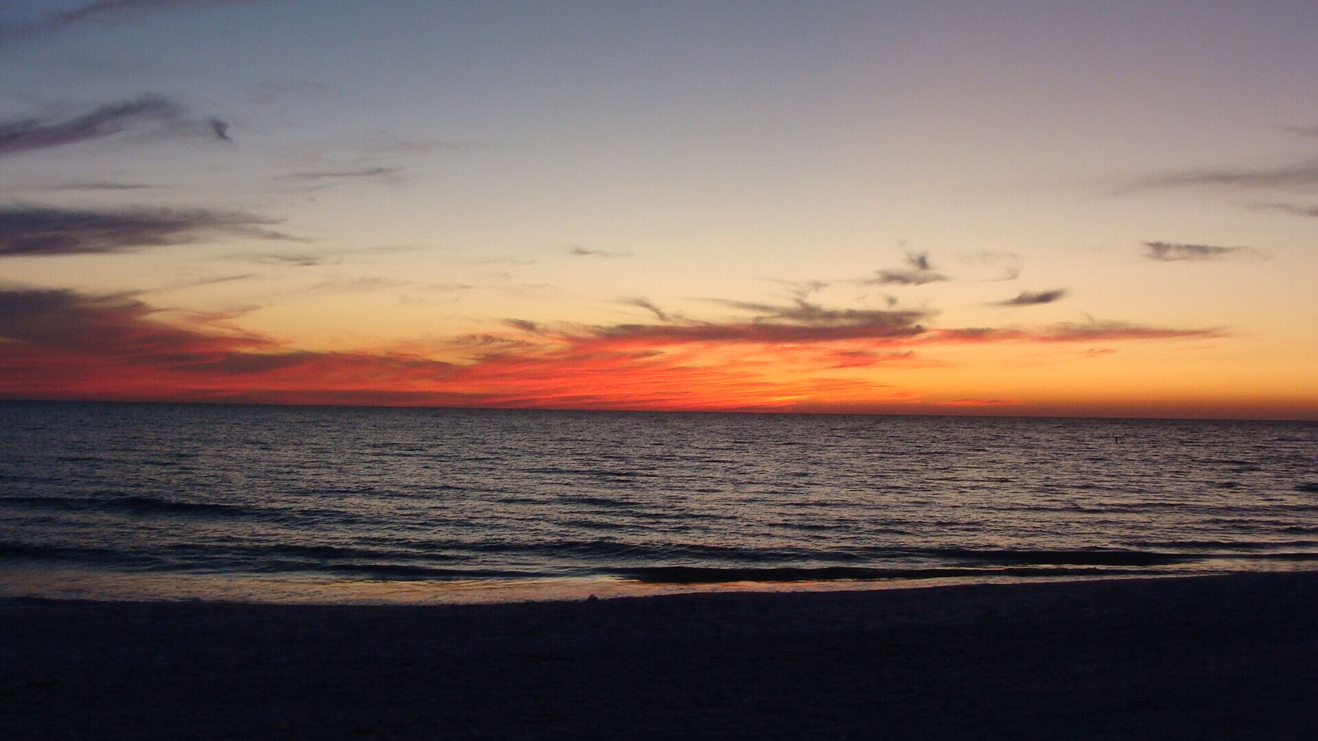 A beach at sunset with calm waves and a clear sky.