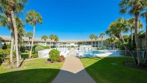 Ein Hotel mit zentralem Pool, umgeben von Palmen und einem gepflegten Rasen.