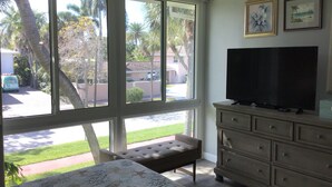 Ein Zimmer mit großem Fenster, einem Fernseher auf einer Kommode und einer Bank.
